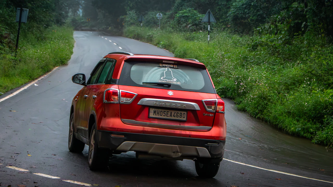 A red car drives down a wet, winding road