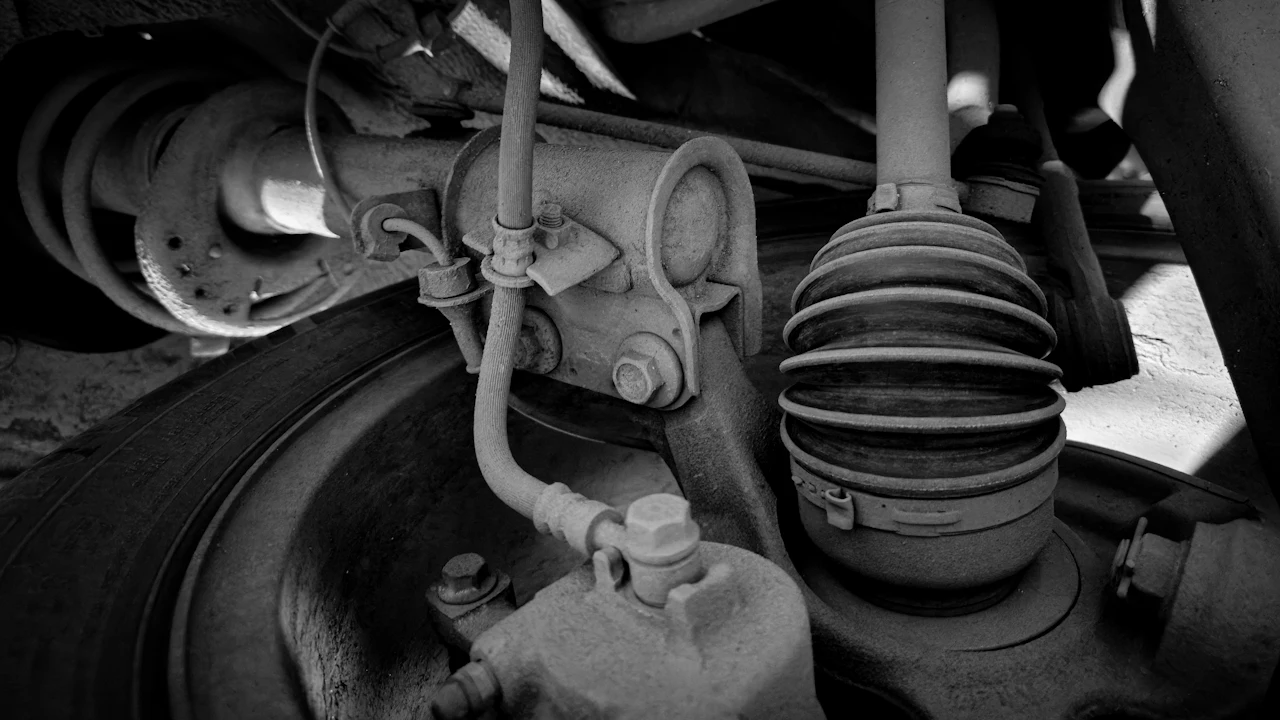 The underside of a car's front suspension — a brake drum, a CV boot, a control arm and joints