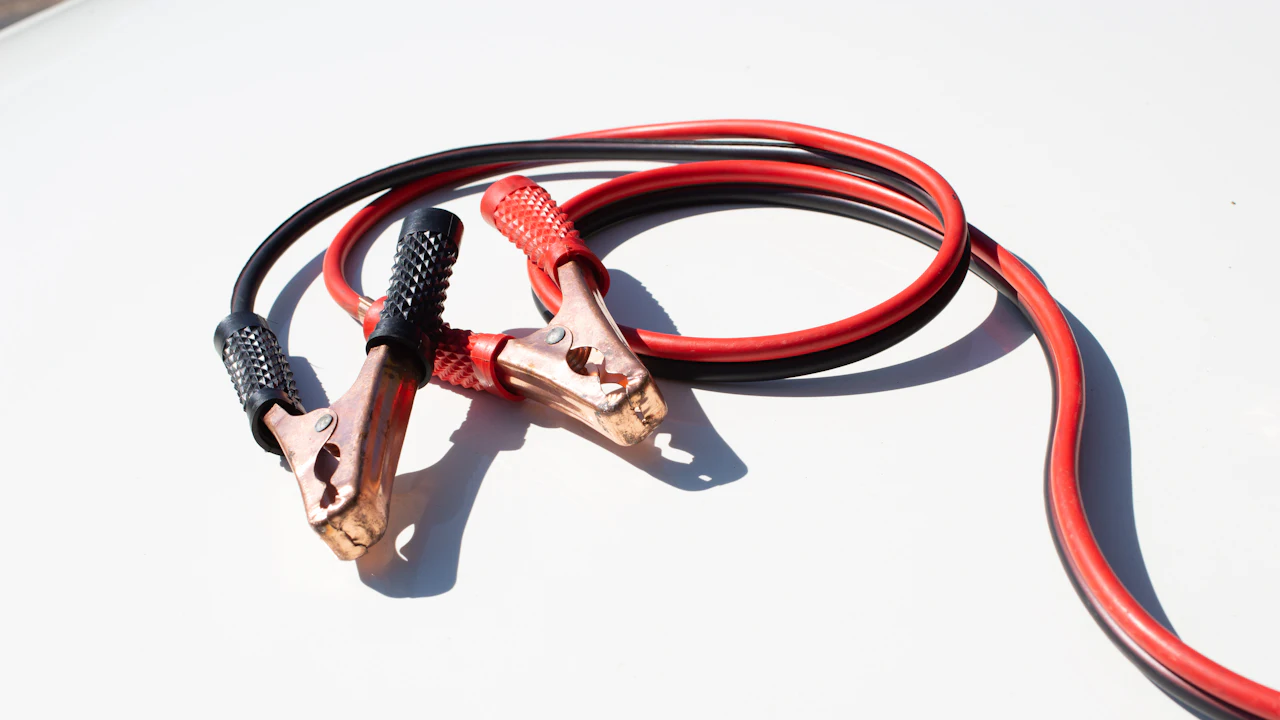 Red and black jumper cables with copper clamps coiled on a white surface