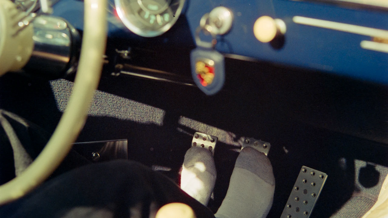 A driver's foot on the brake pedal in a car footwell, pedals and dashboard above