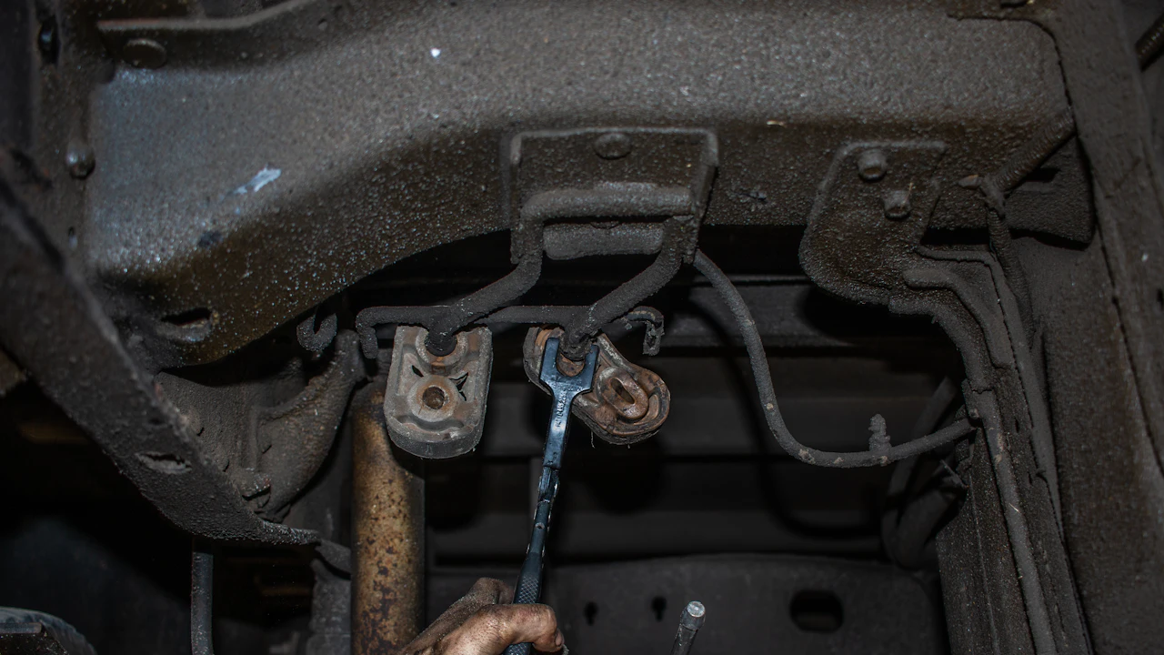 The rusty underside of a car with a hand using a wrench on corroded brake lines and fittings