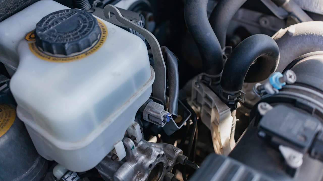 A translucent brake-fluid reservoir and its cap on the master cylinder under a car's hood
