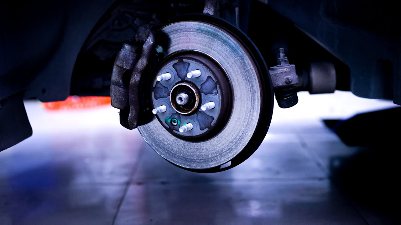 A car's disc brake rotor and caliper on the wheel hub, seen with the wheel removed