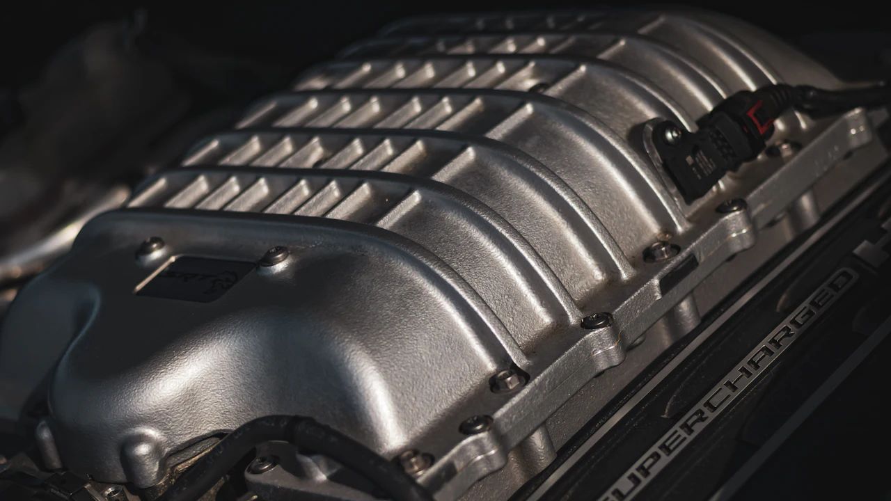 A close-up of a modern car's aluminium intake manifold under the hood, an electrical connector at one side