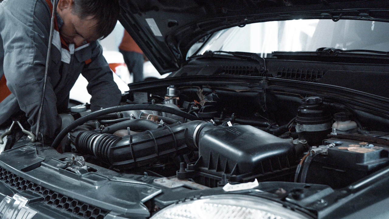 A mechanic leaning into an open engine bay, working on a modern engine under the hood