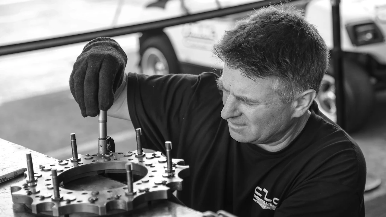 A mechanic working on a metal engine component with a hand tool at a workbench