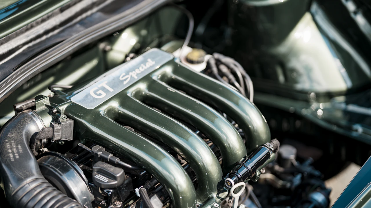 A car engine's intake manifold on top of a green engine under the hood