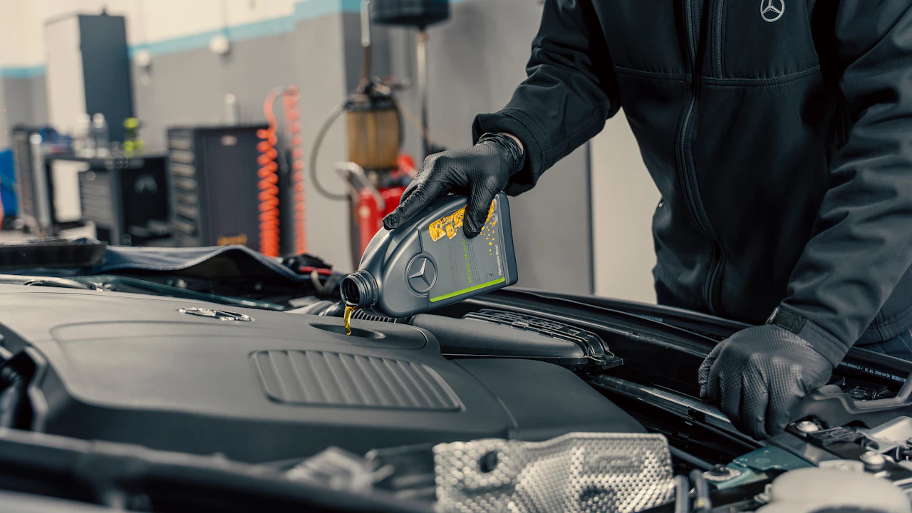 A technician in gloves servicing a car engine under the hood in a workshop