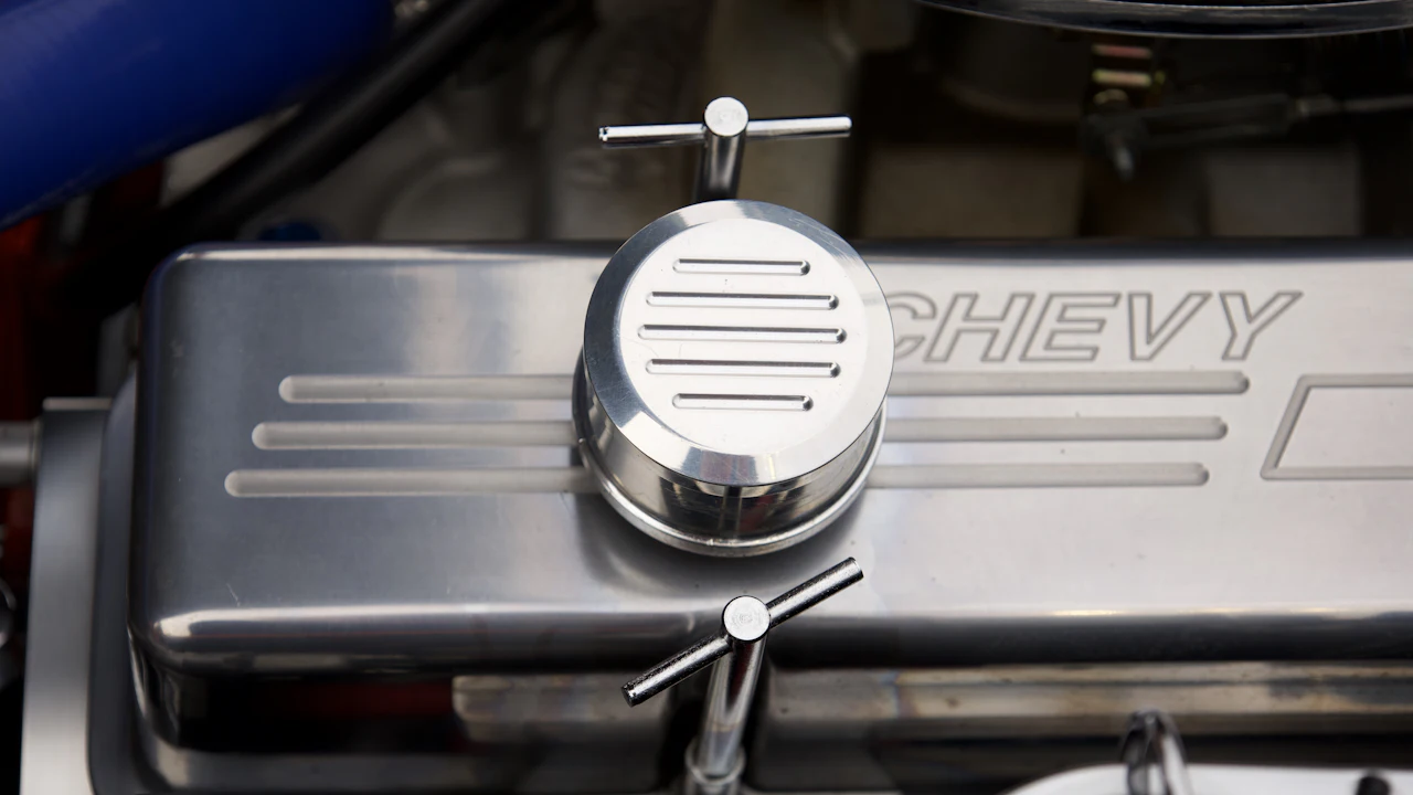 A chromed engine valve cover with an oil filler cap, 'CHEVY' embossed on it