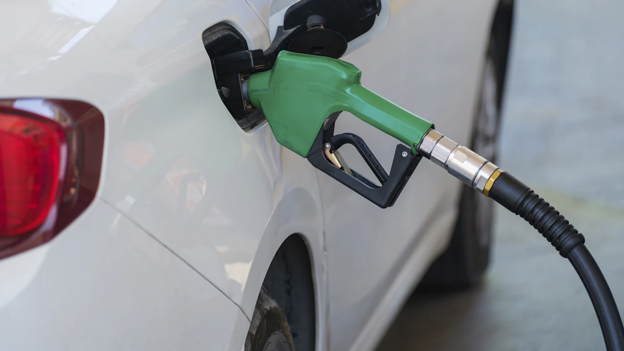 A green fuel-pump nozzle inserted in the filler of a white car at a gas station