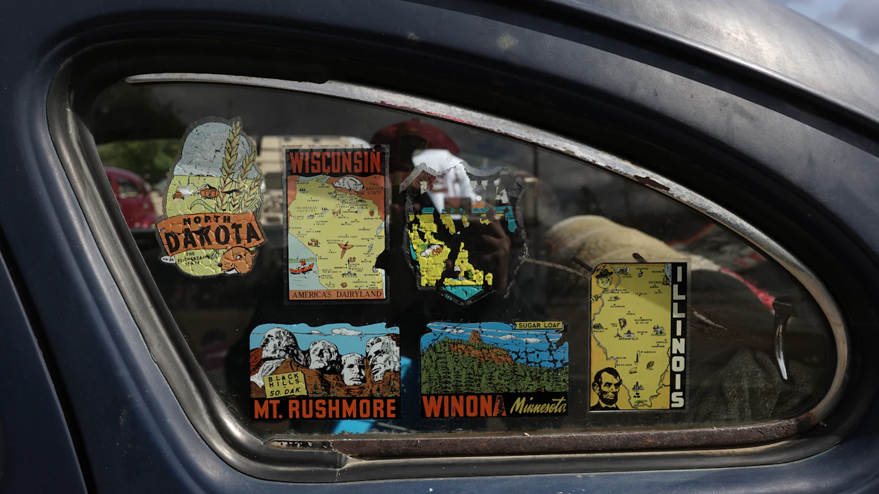 The rear side window of an old car covered in vintage state travel decals for several American states
