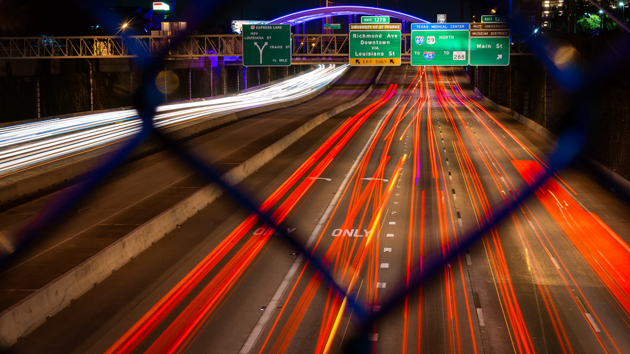A long-exposure view down a Houston freeway at night, red and white light trails under overhead signs for the Texas Medical Center and Interstate 45