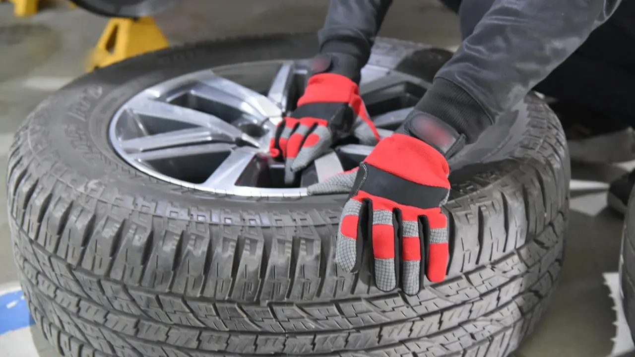 Gloved hands working on a tire and alloy wheel in a shop.