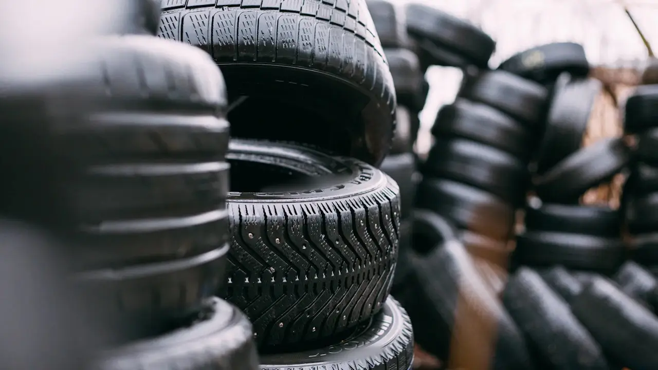 Close view of stacked new tires, the nearest showing its tread blocks, grooves and sidewall; sidewall lettering blurred.