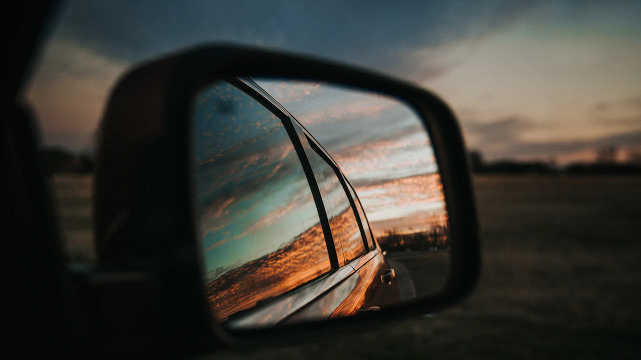 A pickup wing mirror reflecting the road behind at sunset
