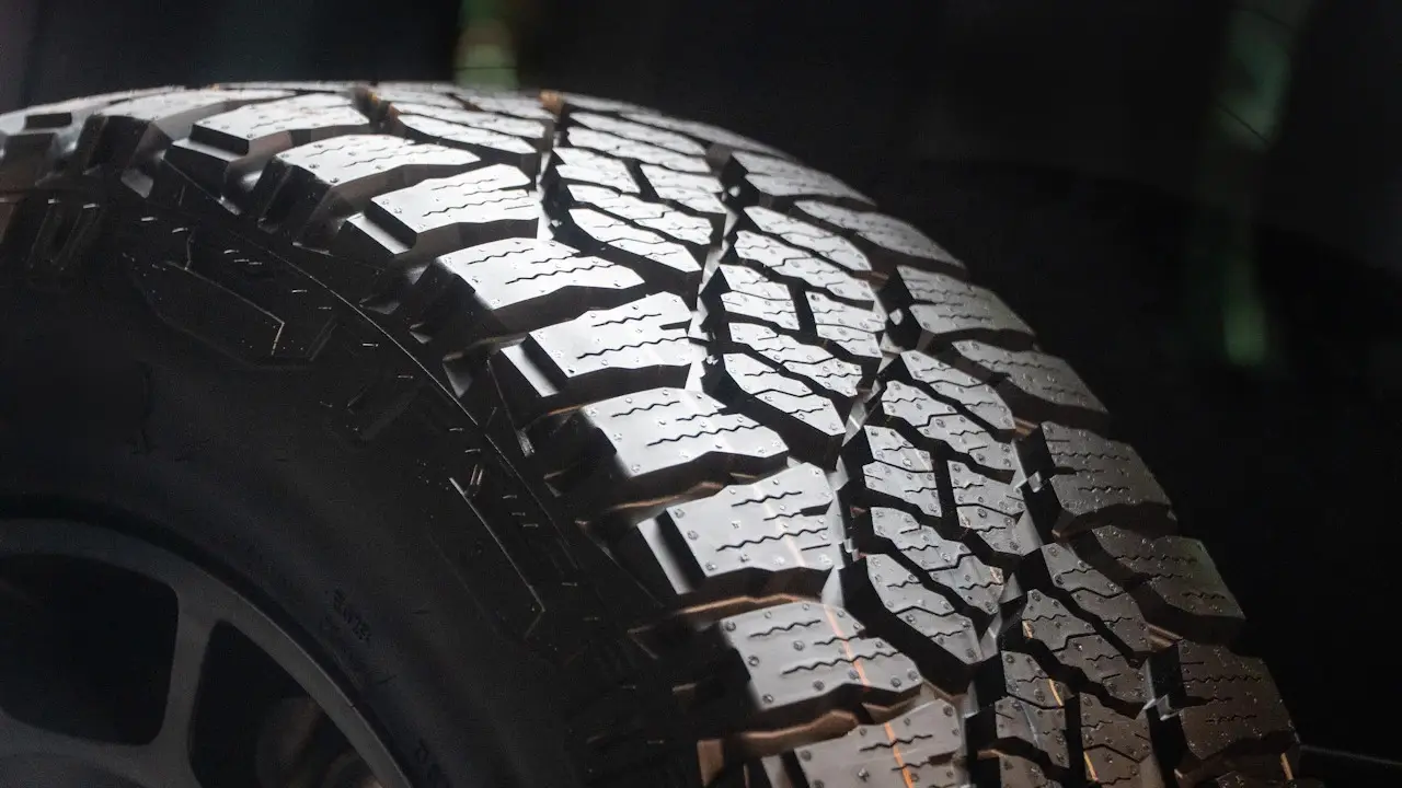 Close view of an all-terrain tire's tread blocks and the edge of its wheel.