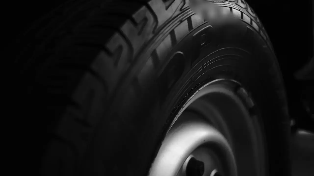 Close view of a tire's tread blocks and sidewall on a steel wheel, in low light; sidewall lettering blurred.