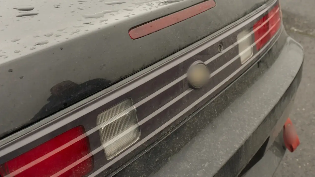 Close view of a dusty car's rear panel, tail lamps and trunk lid.