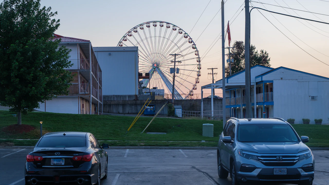 Two cars parked in a motel car park at dusk with a white ferris wheel rising behind the buildings