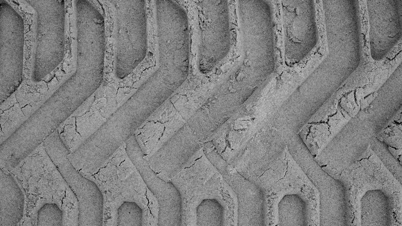 A tyre tread pattern photographed close up, the grooves packed with dried mud