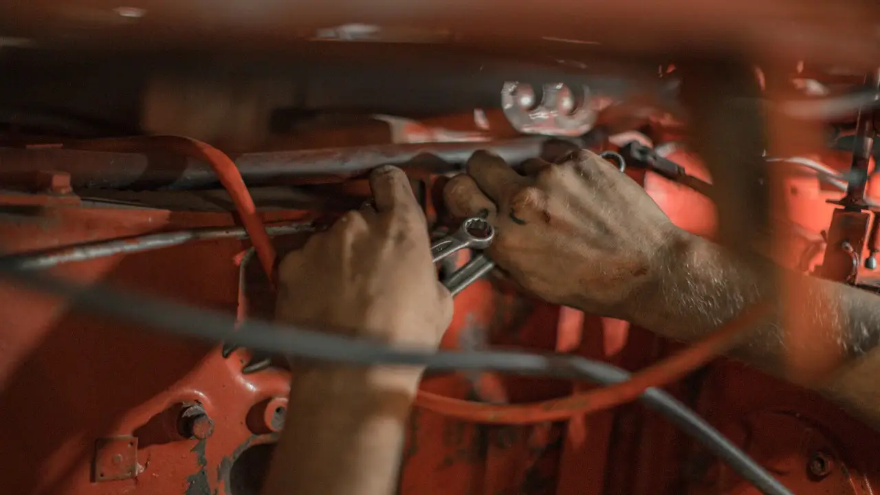 Hands with a wrench working among pipes and cables under a red car.