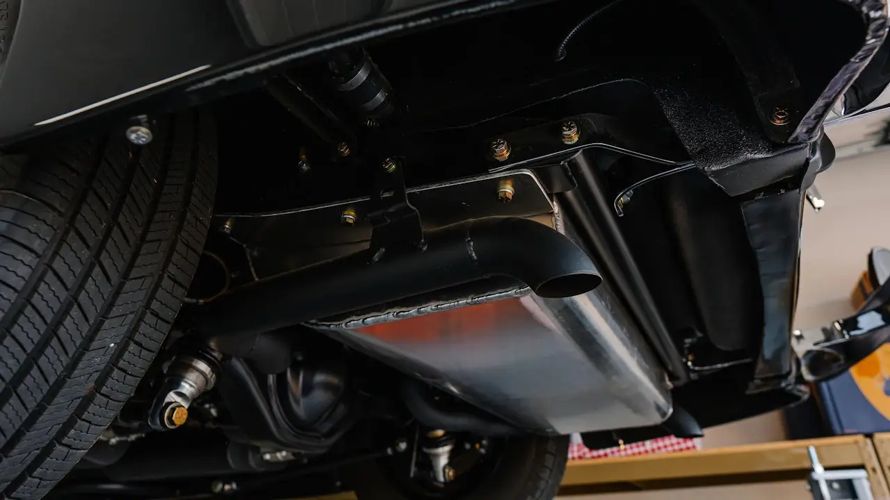 The coated underside of a car on a lift, with its exhaust and frame rail in view.