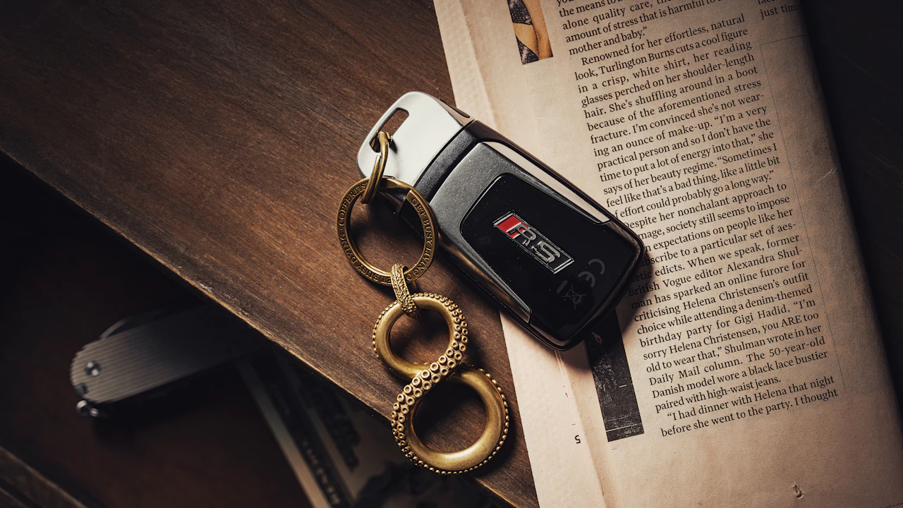 A car key fob with a brass keyring resting on an open book and papers on a dark desk