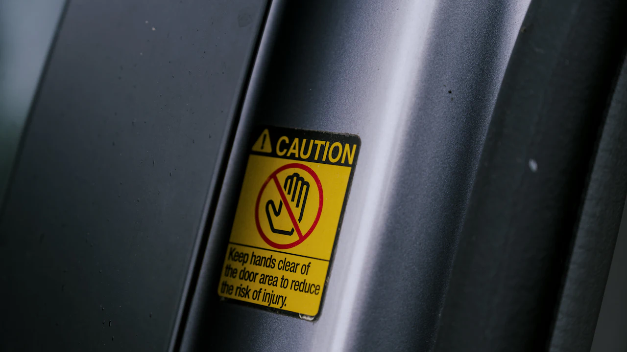 A small yellow warning label stuck to the painted pillar inside an open car door, the door shut line running away behind it
