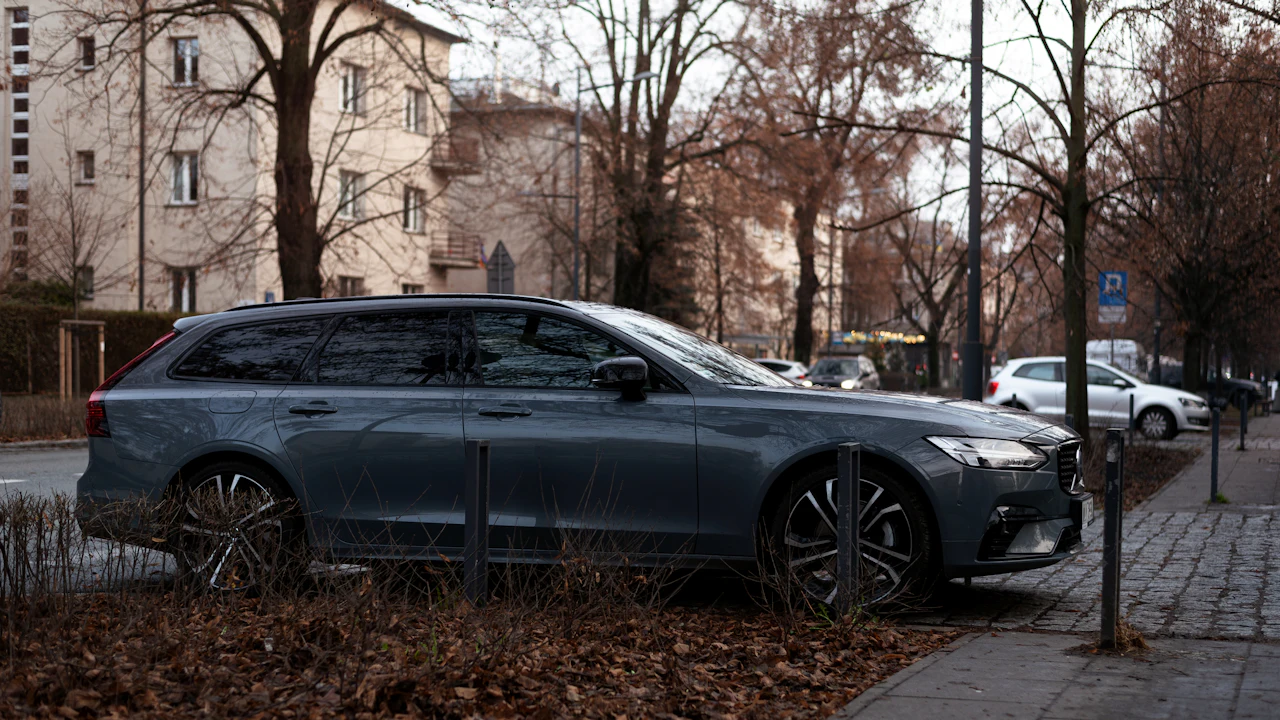 A grey Volvo estate parked at a European kerbside among bare winter trees, apartment buildings behind