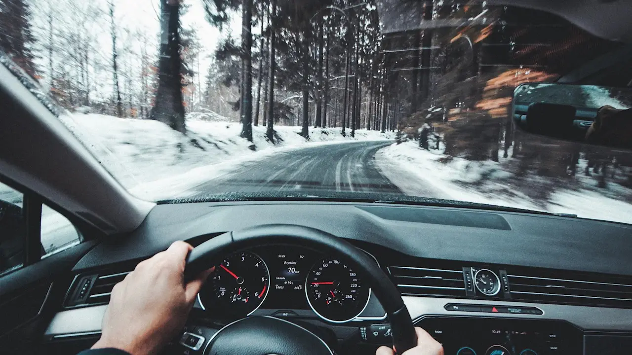 A driver's hands on the steering wheel on a snowy forest road.