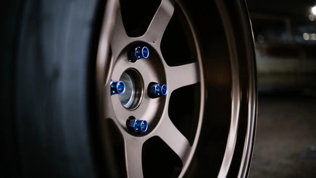 A bronze alloy wheel with blue lug nuts and the tire's sidewall beside it.