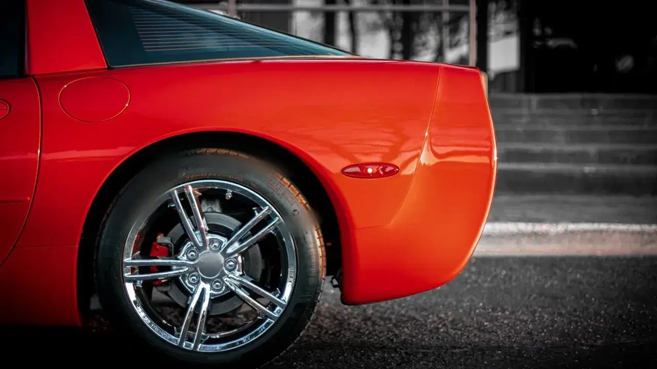 The rear wheel of a red sports car: a chrome five-spoke wheel, the tyre, the brake disc and a red caliper behind the spokes.