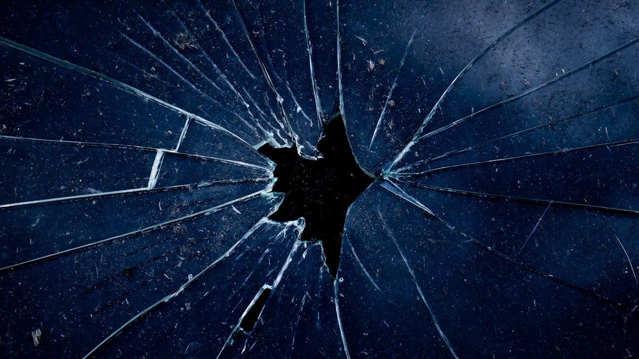 Shattered glass radiating cracks outward from a hole, lit from behind