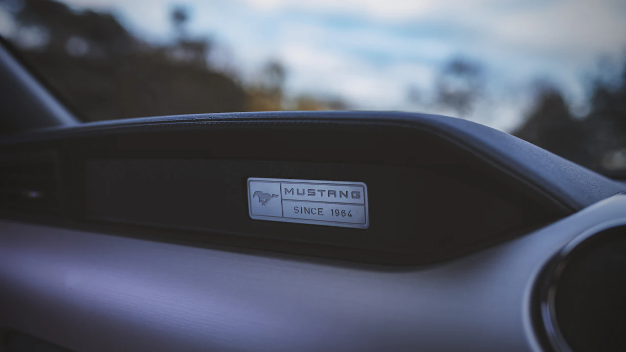 A metal plate set into the top of a car dashboard photographed through the windscreen, carrying a Mustang badge