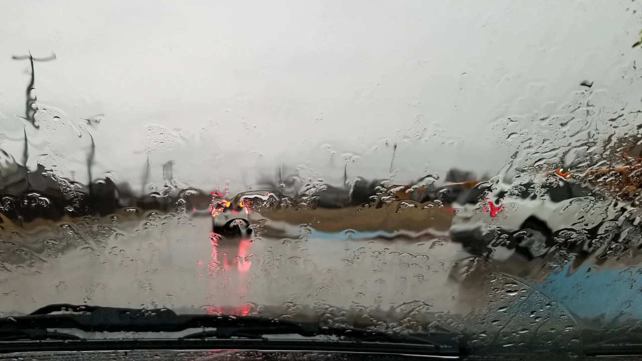 The view through a rain-covered windscreen, wipers mid-sweep and brake lights ahead