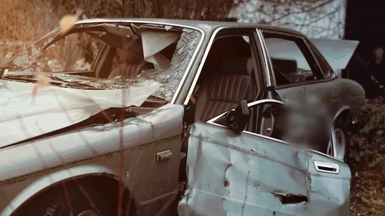 A wrecked grey sedan with a shattered windscreen, its dented driver's door hanging open.